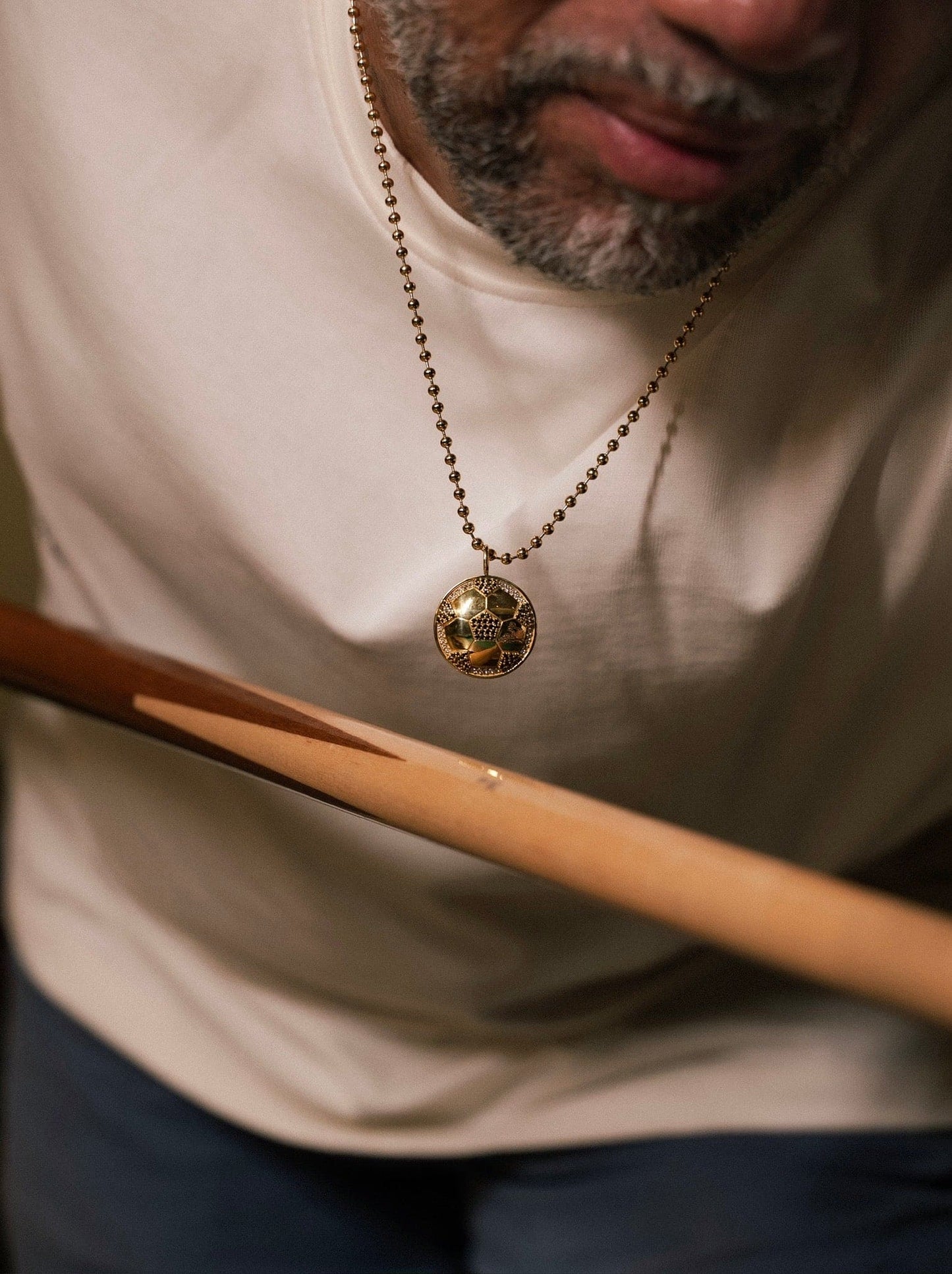 Person wearing a necklace with a gold pendant, holding a wooden object.